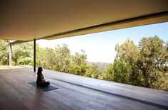 a person sitting on a yoga mat in the middle of a room with large windows