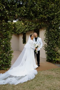 a bride and groom standing in front of an archway with greenery on either side