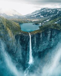 an aerial view of a waterfall in the middle of mountains with a body of water below it