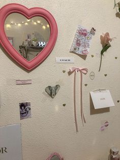 a heart shaped mirror hanging on the side of a wall next to flowers and other items