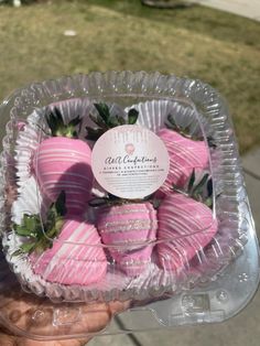 a person holding up a plastic container filled with pink chocolate covered strawberries on top of a sidewalk