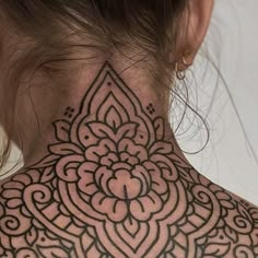 the back of a woman's neck with an intricate tattoo design on her neck