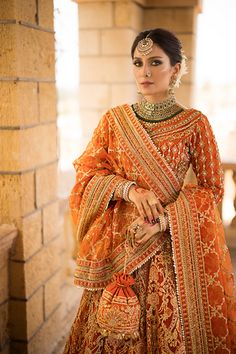 a woman in an orange and gold bridal outfit standing by a brick wall with her hands on her hips