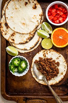 tortillas, limes, peppers, and sliced oranges on a tray