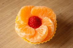 an orange flower made out of fruit sitting on top of a wooden table next to a cupcake