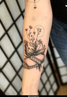 a woman's arm with a book and flowers tattoo on the left inner forearm