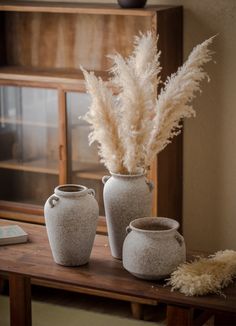 three white vases sitting on top of a wooden table next to a book shelf