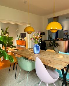 a wooden table surrounded by colorful chairs in a room with yellow and blue lights hanging from the ceiling