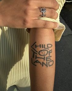 a woman's hand with a tattoo on her arm that reads, child of the land