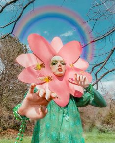 a woman in a green dress holding a large pink flower over her face with a rainbow in the background