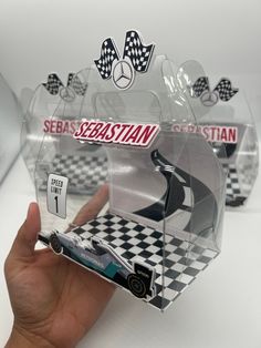 a hand is holding a toy car in a clear plastic case with black and white checkered flooring