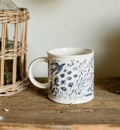 a blue and white mug sitting on top of a wooden table next to a bird cage