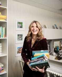 a woman standing in front of a bookshelf with pictures on the wall behind her