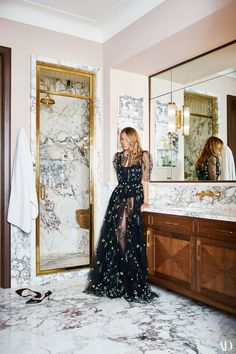 a woman in a black dress is standing in front of a mirror and looking at her reflection