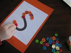 a child's hand is making a letter j craft with buttons on the table