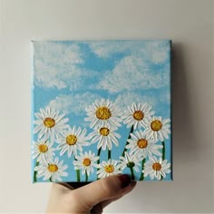 a person holding up a painting with daisies on it