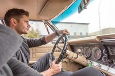 a man sitting in the driver's seat of a car while holding onto his steering wheel