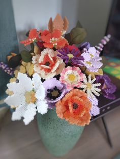 an arrangement of crocheted flowers in a vase sitting on a table next to a chair