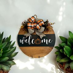 a welcome sign with two pumpkins on it next to some succulents