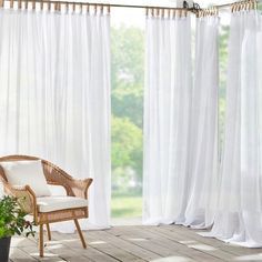 a wicker chair sitting on top of a wooden floor next to a white curtain