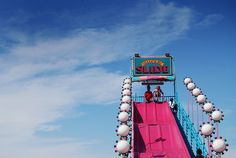 a roller coaster ride with people on the top and bottom deck, in front of a blue sky