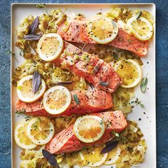 salmon with lemons, onions and herbs on a white platter over blue background