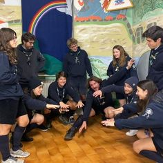 a group of young people standing around each other in front of a wall with pictures on it