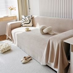 a couch covered with a blanket and pillows next to a pair of slippers on the floor