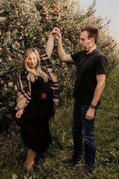 a man and woman standing next to each other in an apple orchard, holding hands