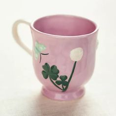 a pink cup with white flowers and green leaves painted on the side, sitting on a table