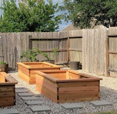 several wooden planters are in the middle of a graveled area near a fence