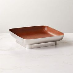 a square metal dish on a marble countertop with a white wall in the background