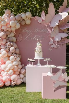 a pink and white birthday party with balloons, cake and cupcakes on the grass