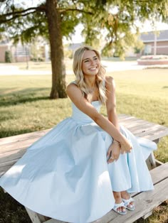 a woman sitting on top of a wooden bench in a park wearing a blue dress