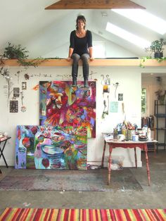 a woman sitting on top of a painting in an art studio