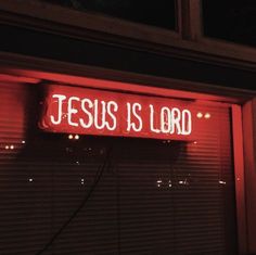 a red neon sign that says jesus is lord on the side of a building at night