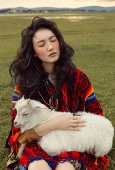 a woman sitting in the grass holding a goat