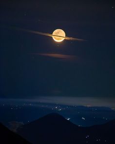 the moon is shining brightly in the night sky above some hills and mountains with lights on them