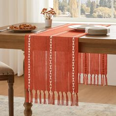 an orange table runner with tassels sits on top of a dining room table