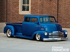 an old blue truck parked in front of a brick building