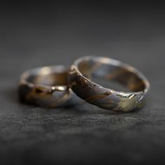 two gold wedding rings sitting on top of a black surface with one ring missing the other