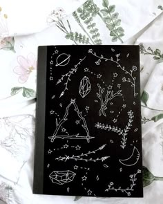 a book with drawings on it sitting on top of a bed covered in flowers and leaves