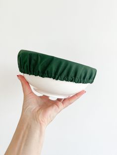 a hand holding a green and white bowl on top of a white tablecloth covered plate