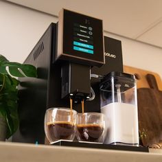 two glasses of coffee sitting next to an espresso machine