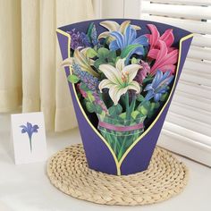 a bouquet of flowers in a vase on a table next to a card and window