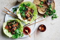 three lettuce wraps on a plate with chopsticks and dipping sauce next to them