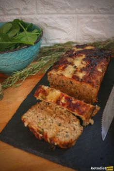 sliced meatloaf sitting on top of a cutting board next to a bowl of greens