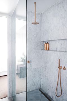 a bathroom with marble walls and floor, gold fixtures on the shower head and hand held faucet