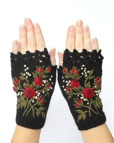 two hands wearing black gloves with red roses on them and green leaves in the middle