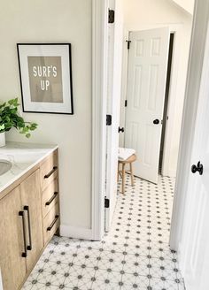 a white bathroom with black and white tile on the floor next to a wooden cabinet